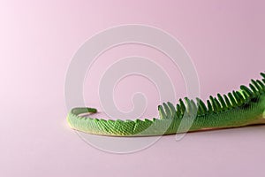 Tail of green lizard toy on pastel pink background. Minimal art concept