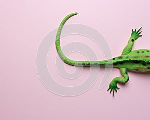 Tail of green lizard toy on pastel pink background. Minimal art concept