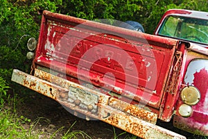 Tailgate of abandoned Vintage red truck parked in a field on a farm