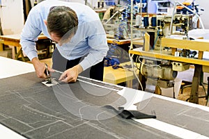 Tailor bending over a workbench cutting fabric