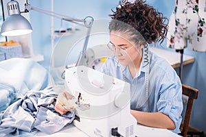Tailor with curly dark hair compliting work with sewing machine at workplace