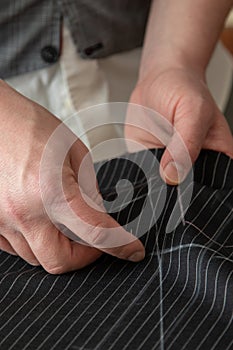 Tailor man working in his tailoring shop, hand sewing dark black wool fabric for suit. Process of hand made bespoke suit with felt