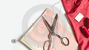 Tailor`s desk. Pattern of clothes and sewing tools. Red cloth, threads, spools, scissors on a white background