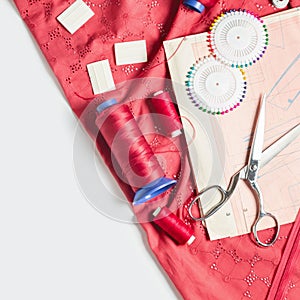 Tailor`s desk. Pattern of clothes and sewing tools. Red cloth, threads, spools, scissors on a white background