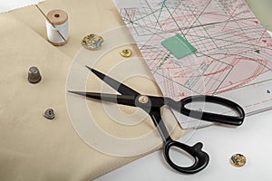Tailor`s scissors lie on a fabric blank against the background of sewing accessories.
