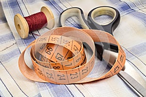 The tailor`s tape measure, a wooden spool of thread and dressmakers scissors on fabric background photo