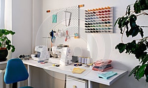 A tailor's workspace in a spacious white room. Large white table with sewing machine and overlock.