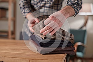 Tailor Selects wool from the stack. Young man working as a tailor and using a sewing machine in workshop.
