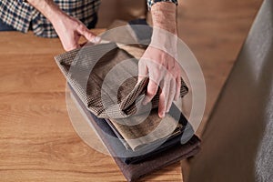 Tailor Selects wool from the stack. Young man working as a tailor and using a sewing machine in workshop.