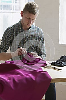 Tailor Sewing Fabric At Table In Studio