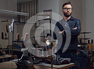 Tailor standing near table with sewing machine and looking at a camera in a sewing workshop.