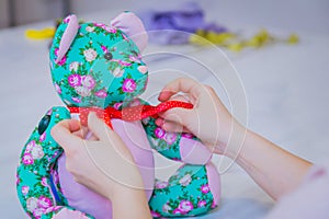 Tailor woman, toymaker tying bow on neck of teddy bear - close up view