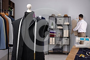 Tailor working in atelier, focus on mannequin with unfinished suit jacket and measuring tape