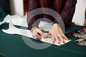 Tailor worktable in studio. Female hands making chalk markings of paper patterns on green fabric.