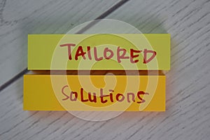 Tailored Solutions write on sticky notes isolated on Wooden Table