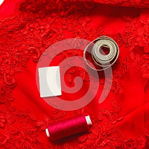 Tailoring concept. elegant fabric white guipure on red guipure with measuring tape and spool