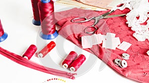 Tailoring. Fashion designer workspace top view. Sewing equipment, colorful thread, red fabric, spools, scissors, pattern on white