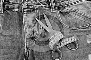 Tailors tools on denim fabric: scissors and yellow measure tape