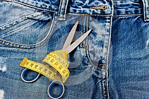 Tailors tools on denim fabric: scissors and yellow measure tape