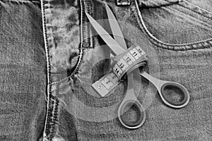 Tailors tools on denim fabric, selective focus. Making clothes and design concept: scissors wound around measure tape