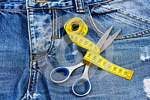 Tailors tools on denim: measure tape wound around metal scissors