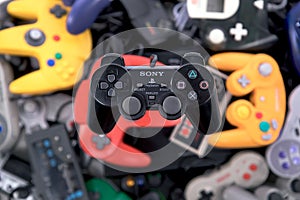 A Sony Playstation 2 Controller Hovering over a Pile of Retro Video Game Controllers
