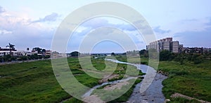 Taiwanese landscape with a river in a green field, buildings in the background