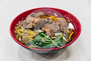 Taiwanese style beef noodle including sliced beef, flat egg noodle, sprouts, morning glory and soup in red bowl