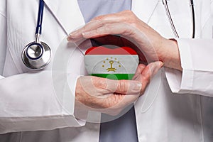 Tajik doctor holding heart with flag of Tajikistan background. Healthcare, charity, insurance and medicine concept