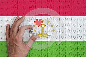 Tajikistan flag is depicted on a puzzle, which the man`s hand completes to fold