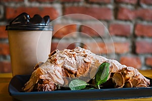 Take away coffee and fresh croissant with mint on wooden background. Cardboard cup with face cap concept