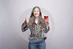 Take away coffee. Happy young woman showing thumb up and holding