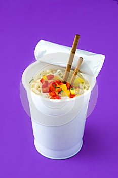 Take away noodles with vegetables on violet background