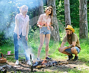 Take a break to have snack. Company hikers at picnic roasting sausages on sticks. Friends prepare roasted sausages