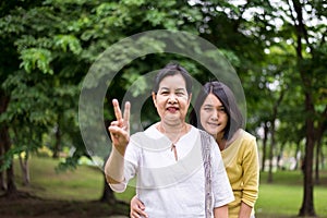 Take care and support concept,Portrait of middle aged asian woman with daughter showing 2 fingers at park together,Happy and smili