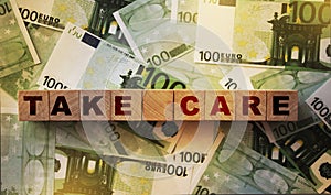 Take care written on a wooden cube on 100 Euro banknotes background. Stay alert and be aware concept