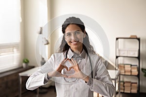 Smiling latin female cardiologist look at camera show finger heart photo