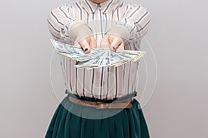 Take it! Close up portrait of successful woman in striped shirt standing, holding many dollars, demonstration fan of money