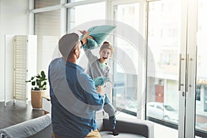 Take this dad. a cheerful little boy and his father having a pillow fight together in the living room at home during the