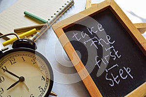 Take the first step phrase colorful handwritten on chalkboard, alarm clock with motivation and education concepts.