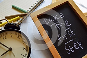 Take the first step phrase colorful handwritten on chalkboard, alarm clock with motivation and education concepts.