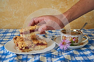 take a homemade pie with jam, a man treats himself to homemade pastries on the table, a man's hand takes a piece of cake