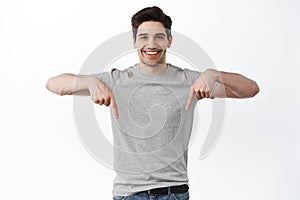 Take a look. Smiling handsome man pointing down and looking assertive, recommend store or promo deal, showing copy space