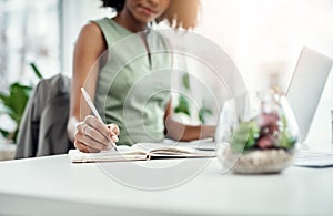 Take note. an unrecognizable young businesswoman writing in her diary while working in the office.