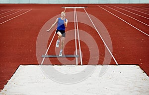 Take off. Focused runner propelling into sand pit. Young man, professional sportsman pushes off ground hard to make a