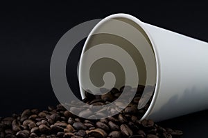 Take-out coffee cup with spilled coffee beans, black background. Coffee beans