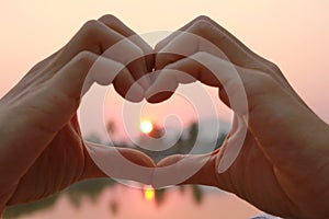 Take photo hands together to form a heart and light from the sun in morning. This photo contain noise and burry