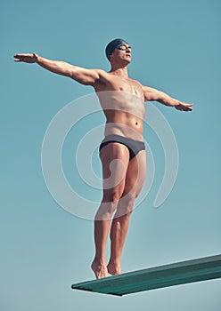 Take the plunge. Full length shot of a handsome young male athlete standing on a diving board outside.