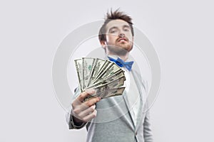 Take it! Portrait of confident attractive young businessman in gray coat and blue bow tie standing, proudly with head up and