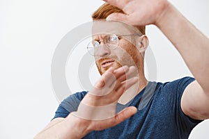 Take this ugly thing away from me. Displeased intense redhead mature guy in glasses and blue t-shirt, turning away and